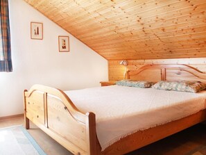 Ein hölzernes Bett in einem Zimmer mit schrägverlaufender Decke und zwei gerahmten Bildern an der Wand.