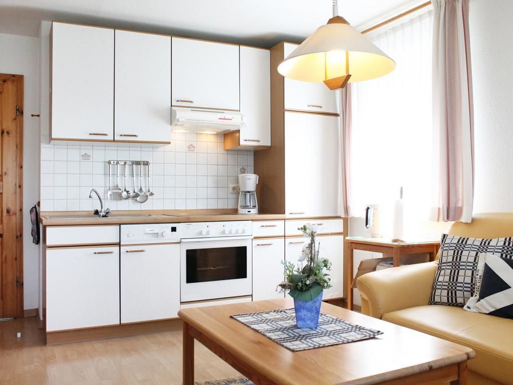 Une cuisine moderne avec des meubles blancs, un plan de travail en bois et une machine à café. On y trouve une table à manger ornée d’un vase de fleurs et d’un set de table à motifs.
