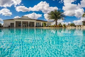 Une piscine à l’eau d’un bleu cristallin, un bâtiment à la façade blanche et aux grandes fenêtres, et un palmier en arrière-plan.