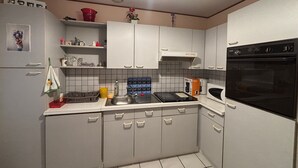 Ett kompakt kök med vita skåp, en spis, en mikrovågsugn och ett handfat.