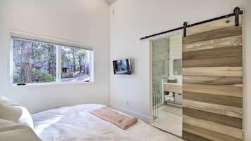 Un dormitorio con cama, ventana con vista a árboles, televisor y puerta corrediza con diseño de paneles de madera.