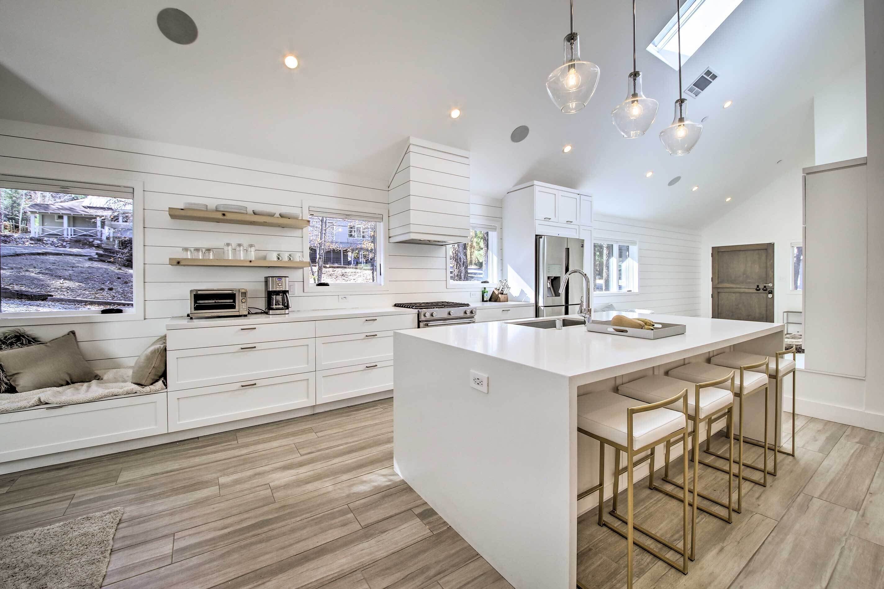 Una cocina moderna con armarios blancos, una isla grande con taburetes de bar e iluminación colgante.