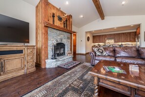 Una sala de estar con chimenea de piedra, armarios de madera, un sofá de cuero y un televisor de pantalla plana.