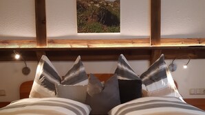 A bed with striped bedding and multiple pillows, a wooden headboard, a small window with a view of a landscape, and wall-mounted lights. - Unterlettlhof (Saalfelden am Steinernen Meer)