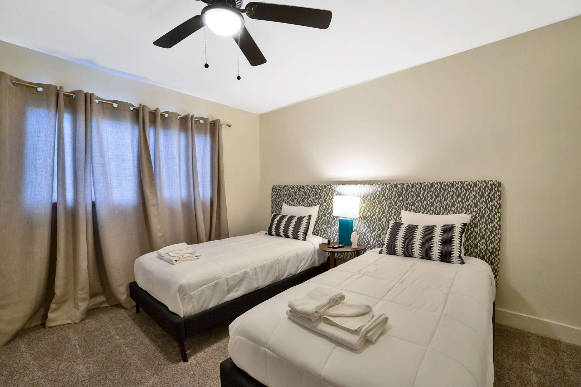 A hotel room with two beds, a ceiling fan, and a nightstand with a lamp.