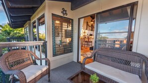 A balcony with wicker furniture, a glass table, and a view of the interior. - North Shore Kauai- AC, pool, lanai; near beaches, golf, walking path to shops (Princeville)