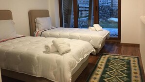 A hotel room with two beds, a view of a stone wall and wooden fence outside, and a patterned rug on the floor. - Meshtekna (Brezovicë)