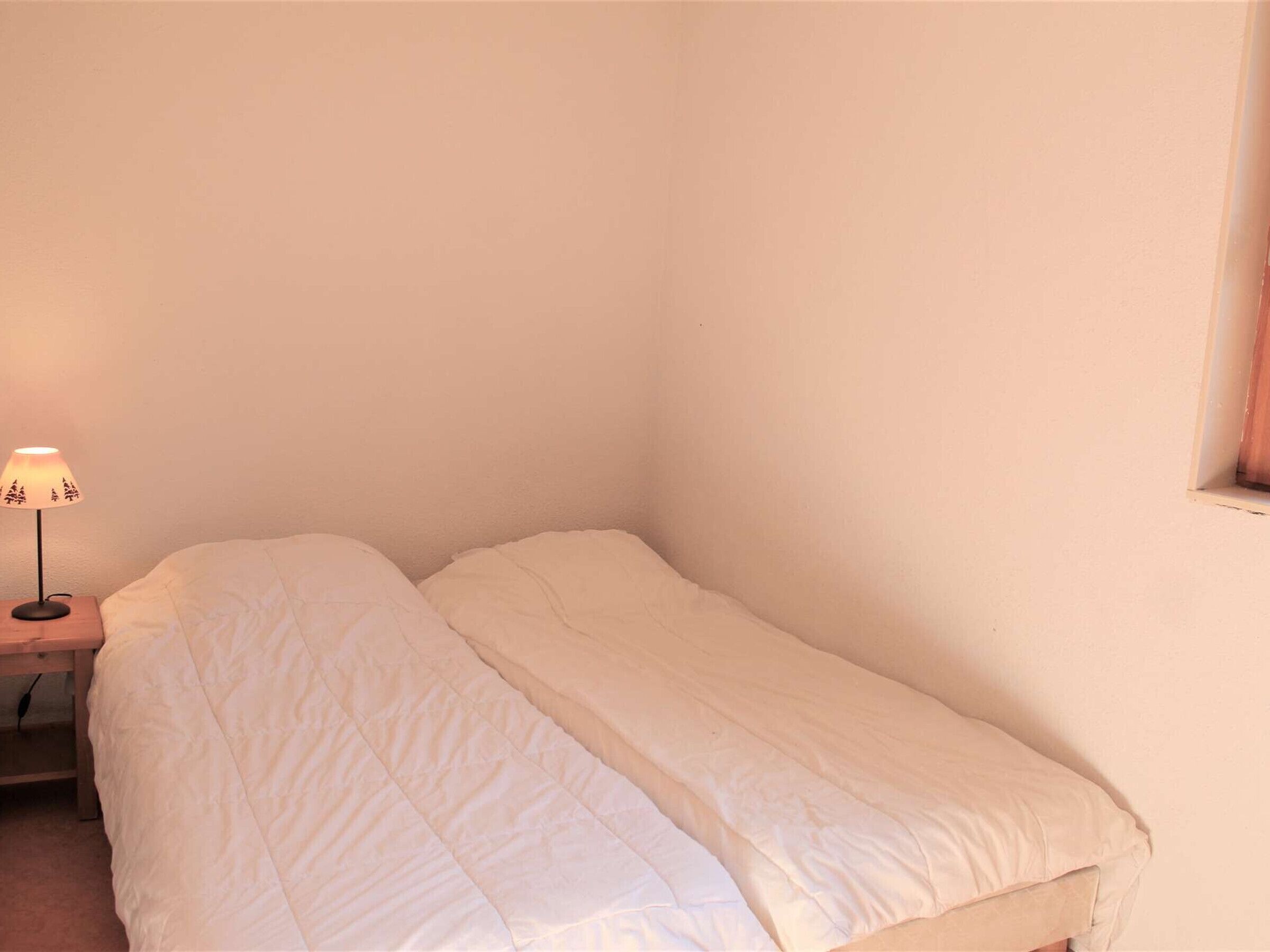 A small, single-bed room with a bedside table and a lamp.