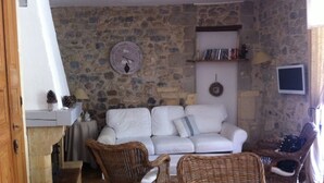 A cozy living room with a stone wall, a white sofa, wicker chairs, and a fireplace. - Character house at the foot of the castle. Shaded terrace (Boulbon)