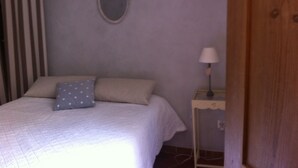 A bedroom with a bed, a nightstand, a lamp, and a window with curtains. - Character house at the foot of the castle. Shaded terrace (Boulbon)