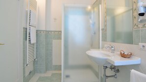 Une salle de bain avec une douche à parois de verre, un lavabo blanc avec un miroir au-dessus, et un porte-serviettes avec une serviette blanche.
