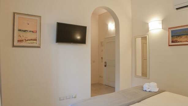 Una habitación de hotel con cama, televisor montado en la pared, un cuadro y un espejo.