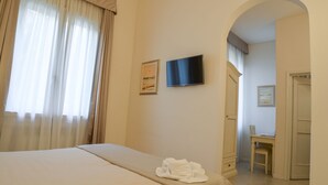 Una habitación de hotel con una cama, un televisor montado en la pared y un escritorio con una silla.