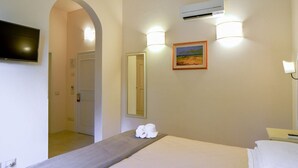Una habitación de hotel con una cama, televisión, un cuadro y un espejo.