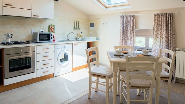 A modern kitchen with a skylight, a washing machine, and a dining area with white chairs and a table. - Apartment with terrace ovelooking Florence (Firenze)