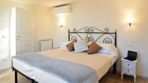 A neatly made bed with a grey bedspread, a white duvet, and two pillows. There is a small bedside table with a laptop and a wall-mounted light. - Apartment with terrace ovelooking Florence (Firenze)