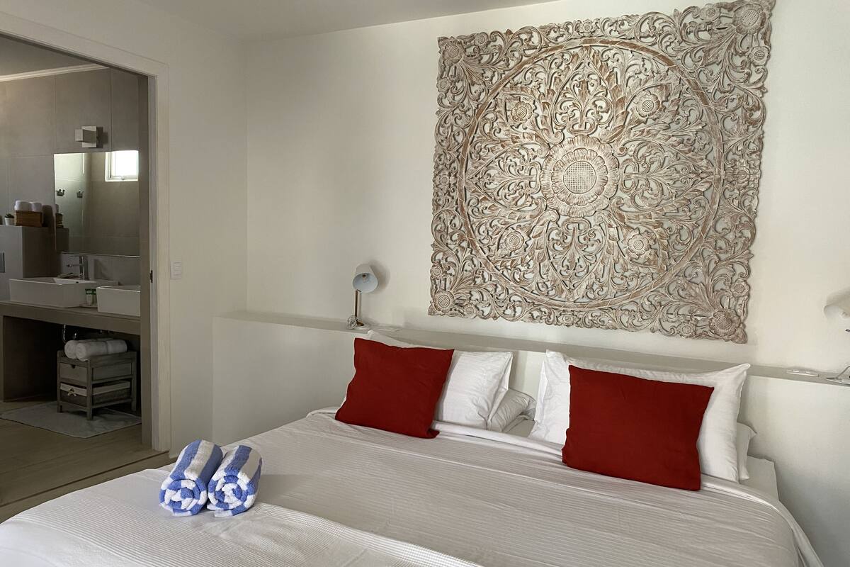 A hotel room with a large bed, a bathroom with a mirror, and a decorative tapestry on the wall.