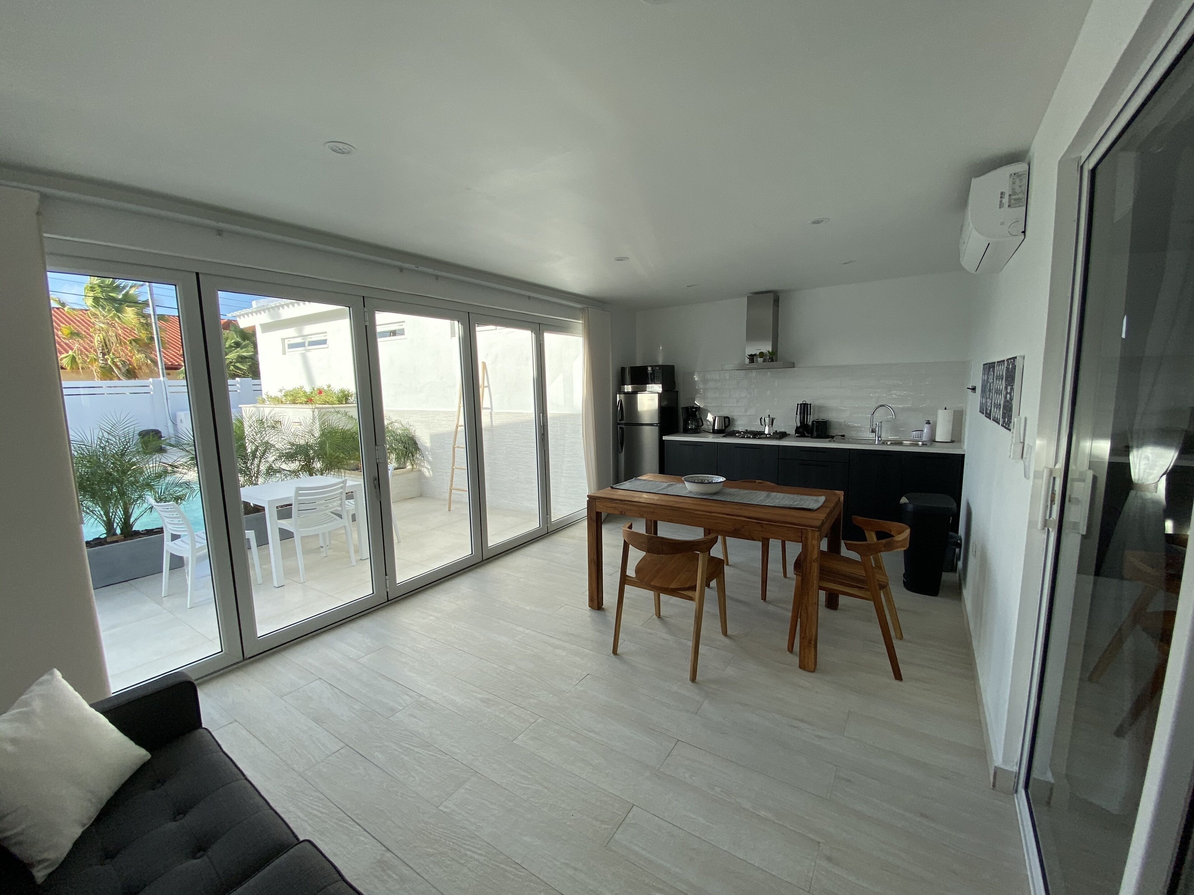 A modern kitchen with a dining area, large sliding glass doors leading to a patio, and a sofa in the foreground.