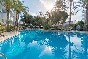A swimming pool surrounded by palm trees and lounge chairs, with a clear sky above. - Aparthotel Tropicana (Son Servera)