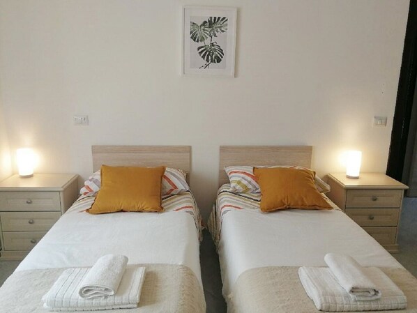 A double room with two beds, each with a headboard, a nightstand, a lamp, and a folded towel on the bed.