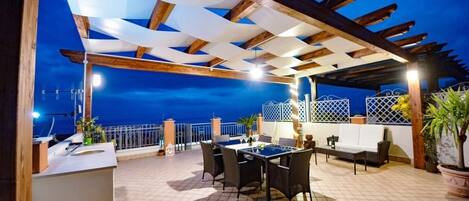 An outdoor patio with a table and chairs, a bar area, and a view of the sea.