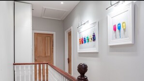 A hallway with a wooden door, a staircase with white balusters, and framed artwork on the walls. - Stylish Double en suite bedroom in Crouch End (London)