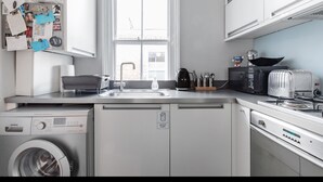 A modern kitchen with a washing machine, dishwasher, and a window with a view of the outside. - Stylish Double en suite bedroom in Crouch End (London)