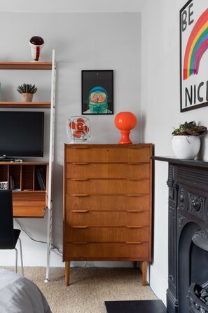 A room with a wooden dresser, a television on a stand, a fireplace, and a framed artwork on the wall.