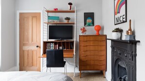 A bedroom with a wooden wardrobe, a desk with a television, a fireplace, and a wall with a rainbow poster. - Stylish Double en suite bedroom in Crouch End (London)