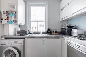 A modern kitchen with a washing machine, dishwasher, and a window with a view of the outside. - Stylish Double en suite bedroom in Crouch End (London)
