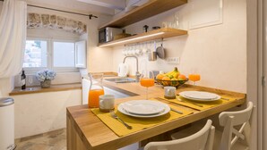 Une cuisine avec une table en bois mise pour le petit-déjeuner, un évier et une fenêtre avec des rideaux.