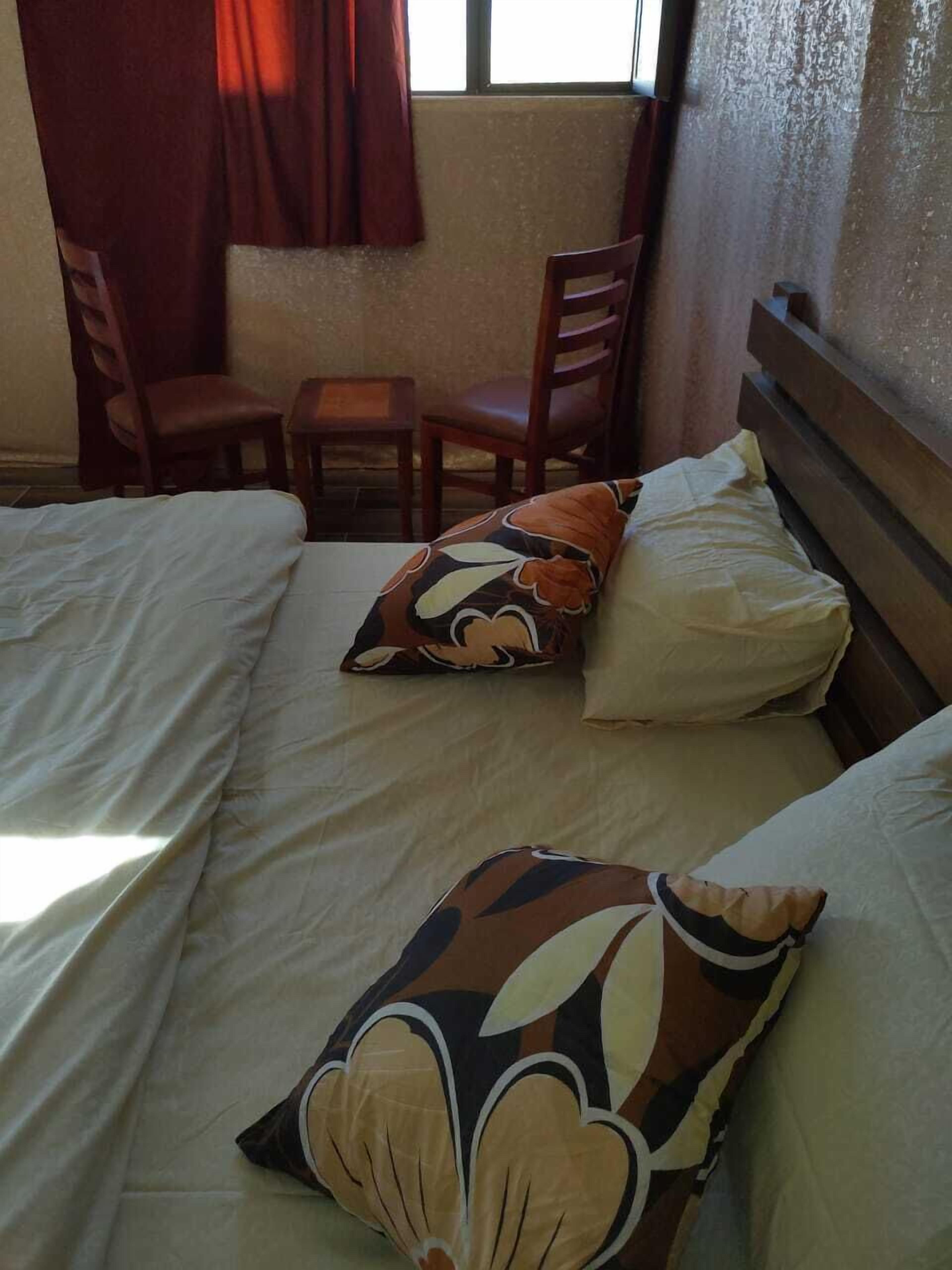 A hotel room with two beds, a wooden headboard, a small table, and two chairs.
