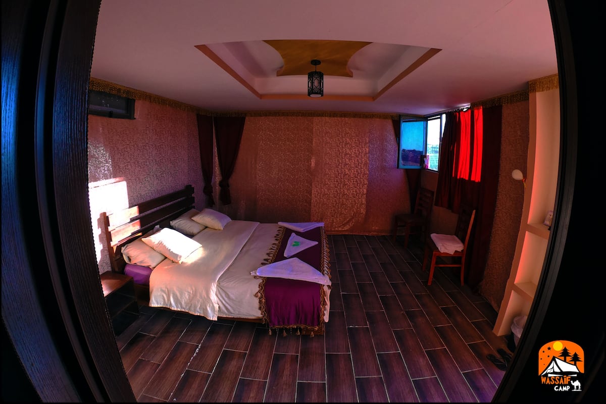 A room with a bed, a chair, a window, and a ceiling light.