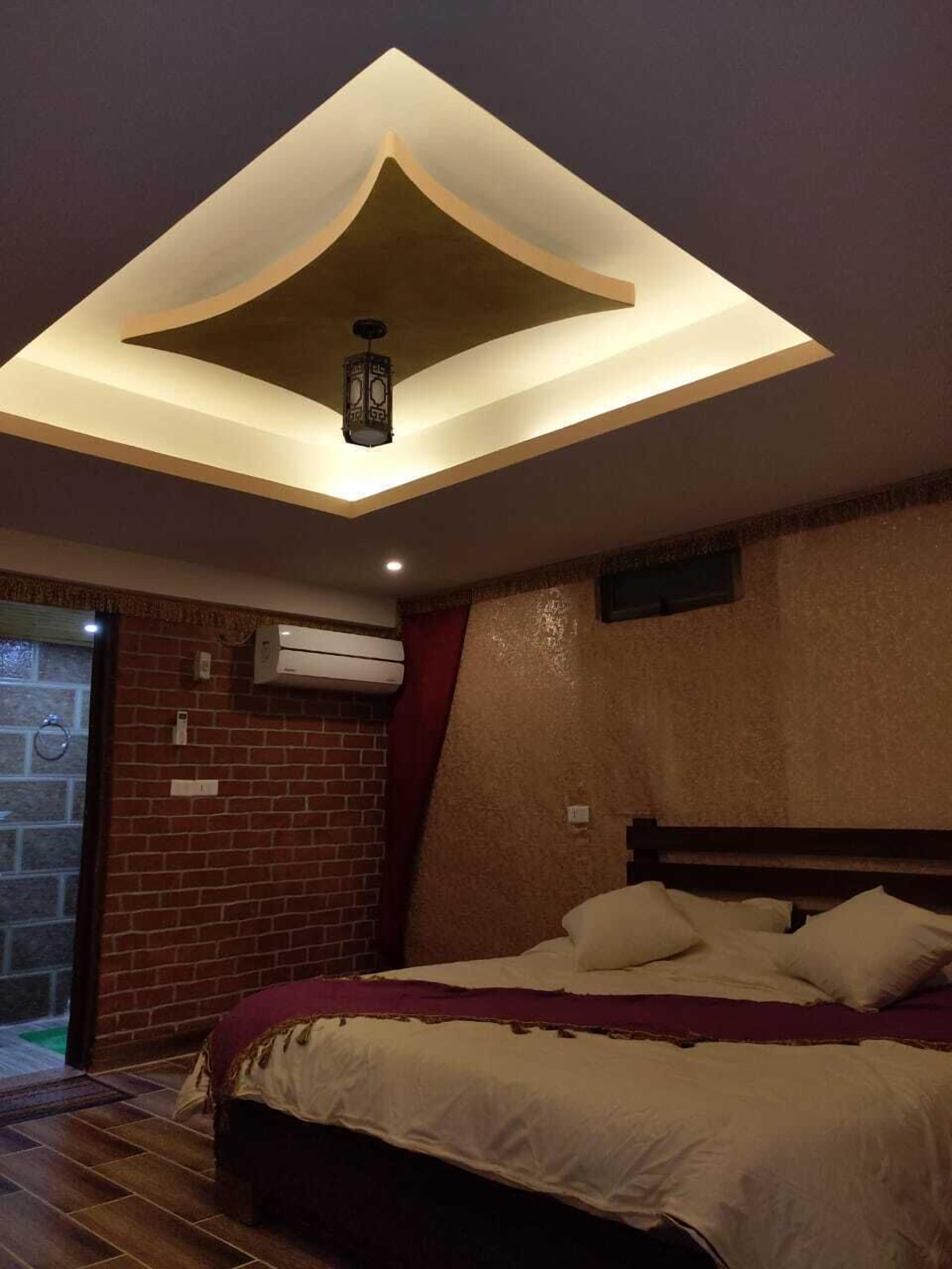A bedroom with a bed, a ceiling light fixture, and a brick wall.