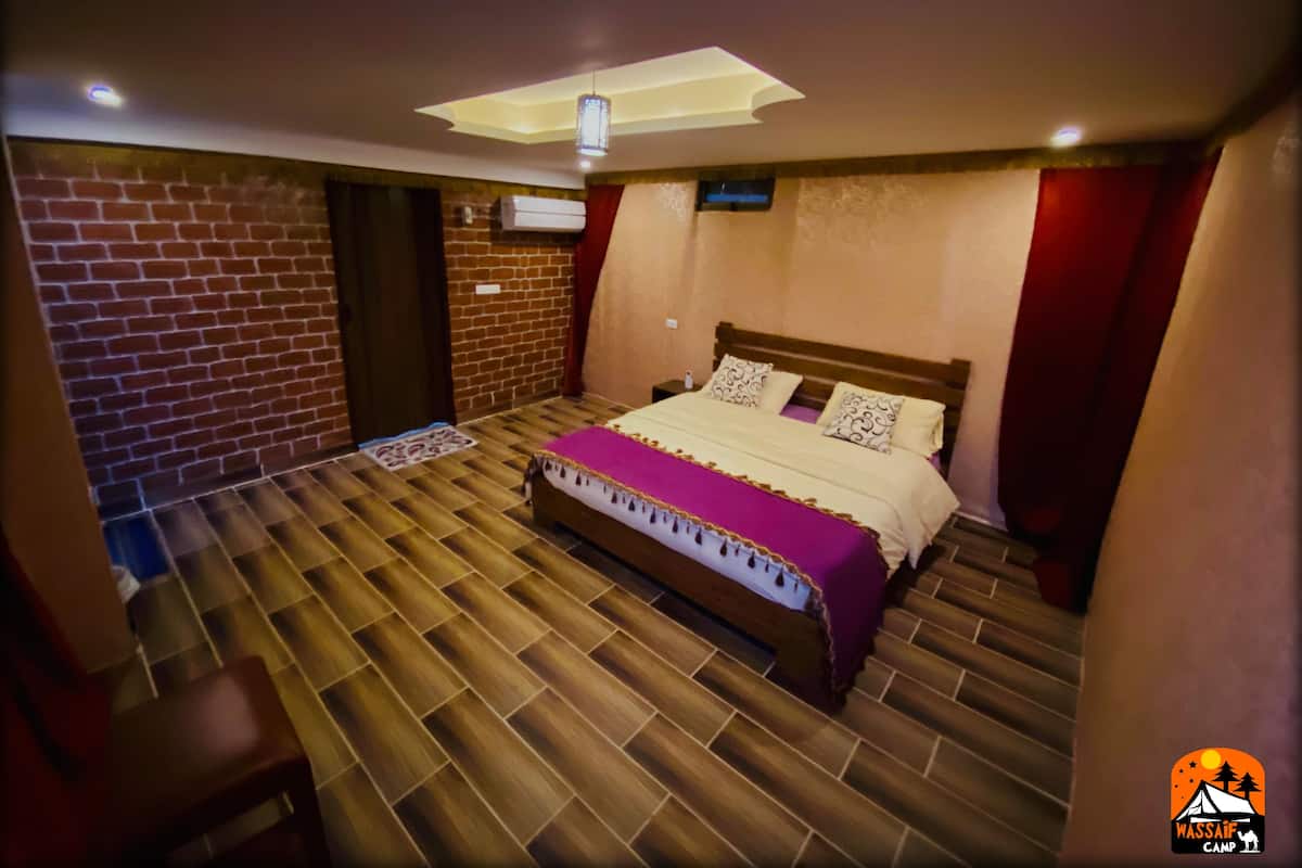 A bedroom with a bed, a wooden floor, a brick wall, and a ceiling light fixture.