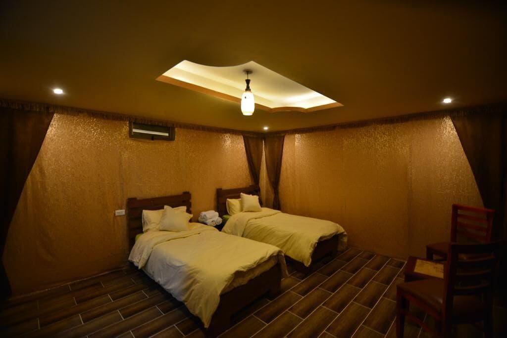 A room with two beds, a ceiling light, and a chair.