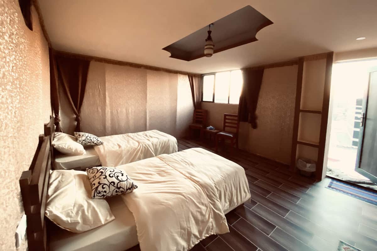 A bedroom with two beds, a ceiling fan, a window, and a chair.