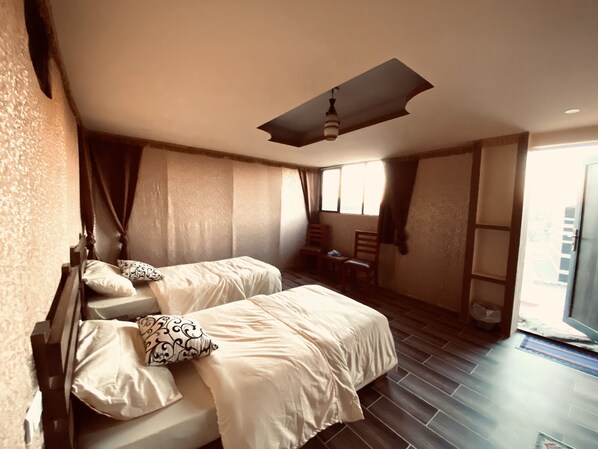 A bedroom with two beds, a ceiling fan, a window, and a chair.
