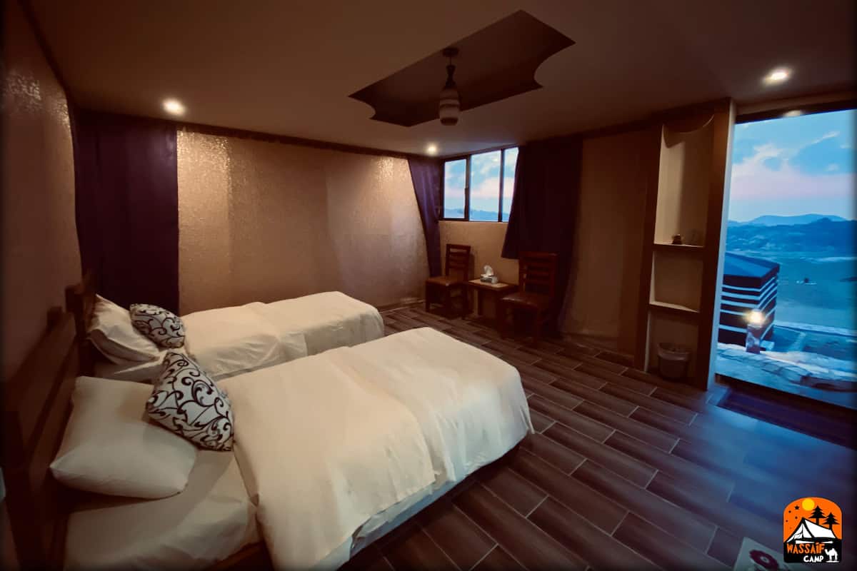 A hotel room with two beds, a small table, chairs, a ceiling fan, and a view of the mountains.
