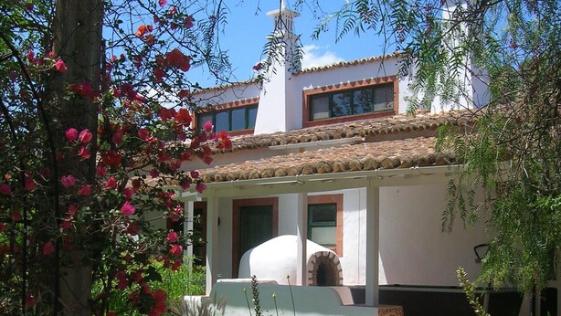 A house with a tiled roof, a chimney, and a garden with flowering plants. - Fazendinha (Tavira)