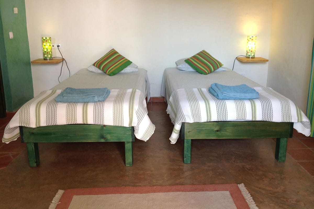 Two single beds with striped bedding, green headboards, and matching pillows. Each bed has a small bedside table with a lamp.