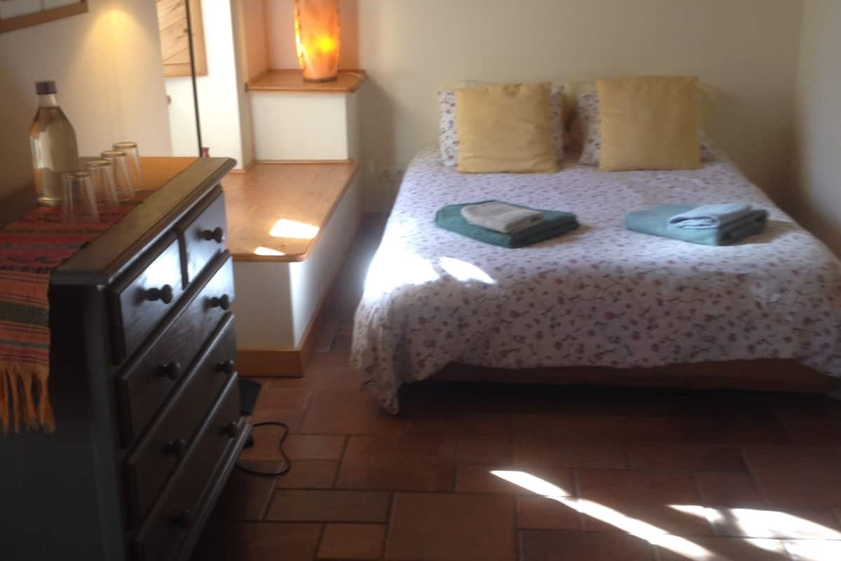 A bedroom with a bed, a dresser, a lamp, and a painting on the wall.