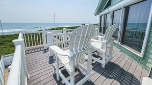 A wooden deck with white Adirondack chairs and a glass railing overlooking the ocean. - Serendipity - Oceanfront, Duck, 5 BR, 4.5BA, Private Pool & Hot Tub (Duck)