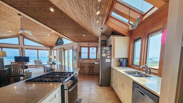 A spacious kitchen with a large island, wooden ceiling, and large windows offering ocean views. - Serendipity - Oceanfront, Duck, 5 BR, 4.5BA, Private Pool & Hot Tub (Duck)