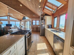 Cozinha ampla com uma ilha grande, teto de madeira e grandes janelas com vista para o oceano.