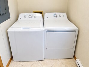 Two white front-loading washing machines in a laundry room with tiled flooring and a wooden door.