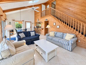 A spacious living area with a high ceiling, wooden walls, a staircase, and a dining area.