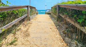 A wooden boardwalk leading to a beach with a lifeguard tower in the distance. - BO DUCK - 3 BR Oceanside Home in the Heart of Duck - Perfect For A Small Family (Duck)