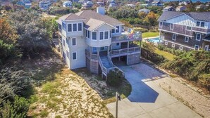 A multi-story residential building with a central courtyard, surrounded by dense vegetation and a distant water tower. - Luzon - 5 BR, 4.5 BA, Oceanside home in Duck w/Private Pool (Duck)