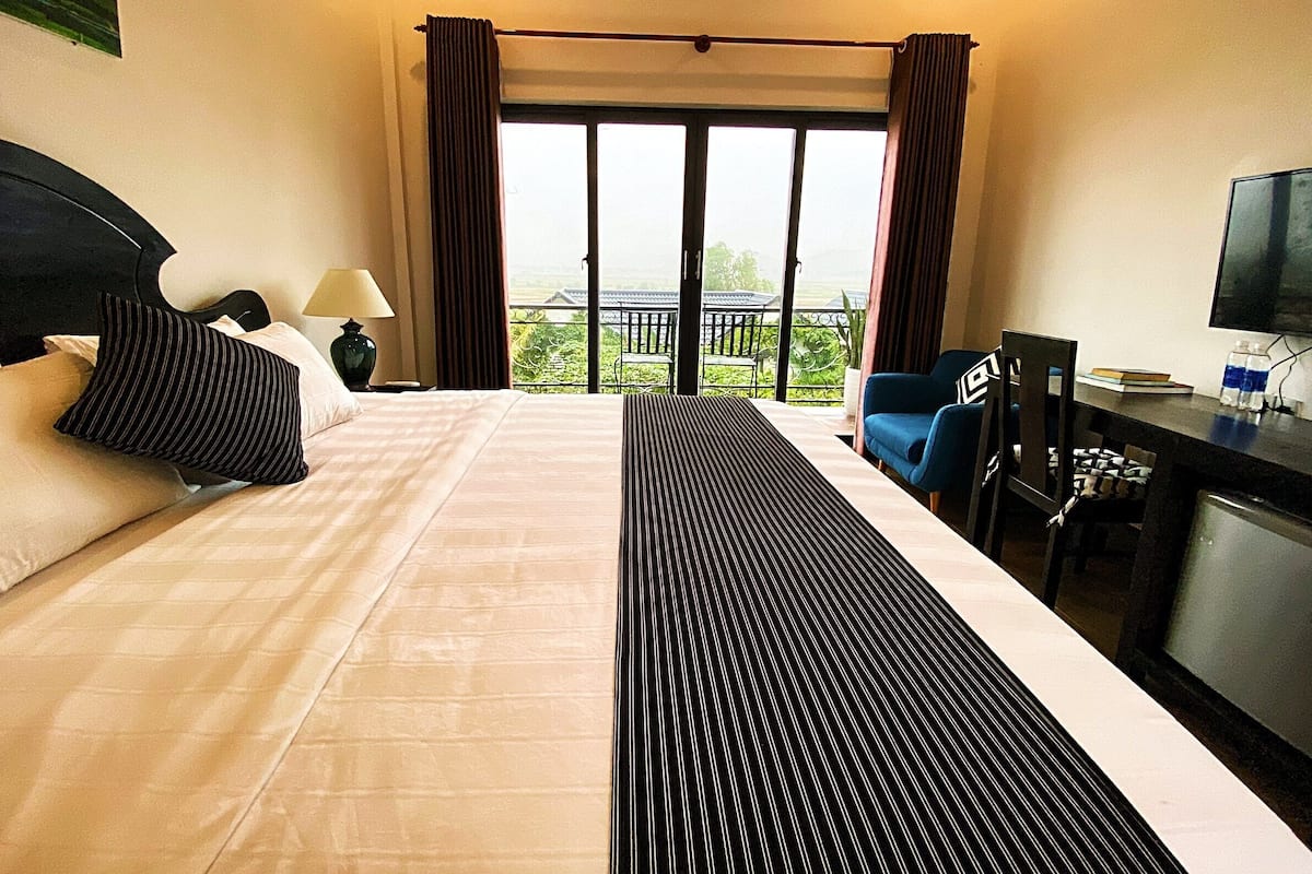 Habitación de hotel con una cama grande, un escritorio con televisor y un balcón con vistas.